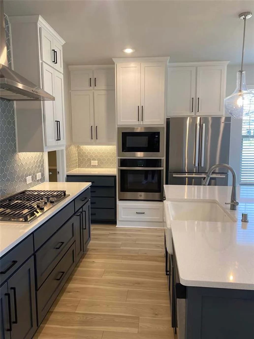 This is an image from Fresh Coat Painters of Wichita.The image shows a modern kitchen with freshly painted cabinets, combining crisp white upper cabinets and deep navy lowers. The updated paint finish complements the stainless steel appliances, tiled backsplash, and light wood flooring.
