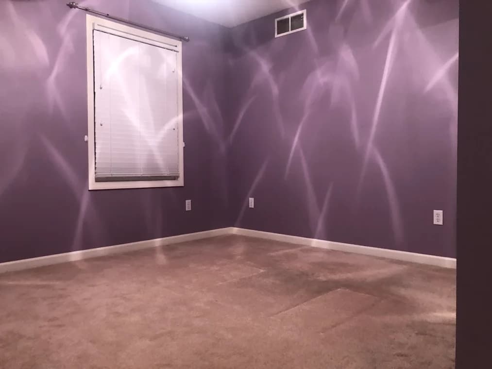 This is an image from Queen City Painting & Wash, located in Ohio. The interior room displays purple painted walls with light reflections creating soft patterns across the surfaces.