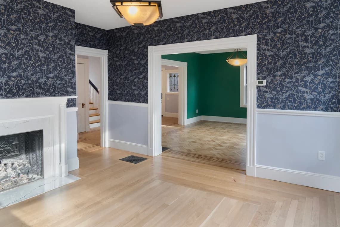 This is an image from Gonnella Painting & Restoration, located in Massachusetts. It highlights an interior room with patterned blue wallpaper, a white fireplace, and adjacent green and light blue painted rooms.
