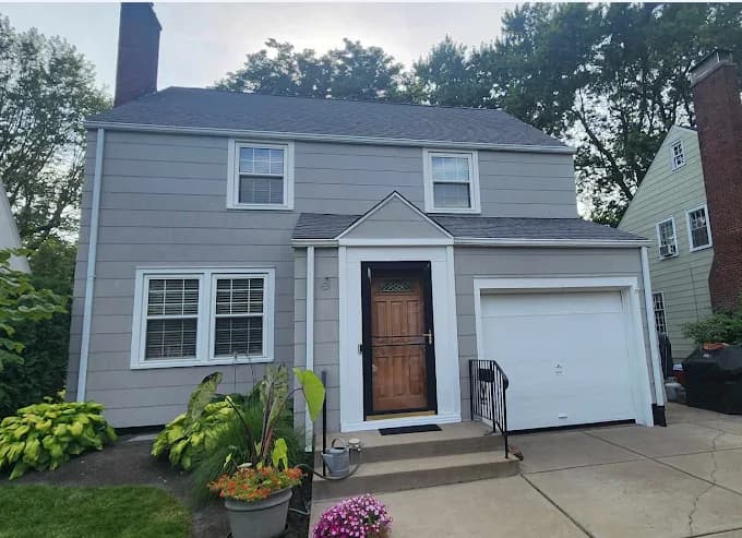 This is an image from Carrigan Painting, located in Wisconsin. The image shows a freshly painted residential home exterior with gray siding, white trim, and a clean, finished curbside appearance.