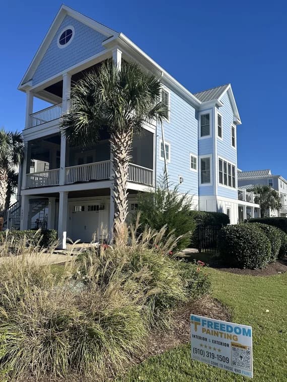 Exterior painting project by Freedom Painting in Wilmington, NC. The image shows a light blue coastal home with balconies and palm trees.