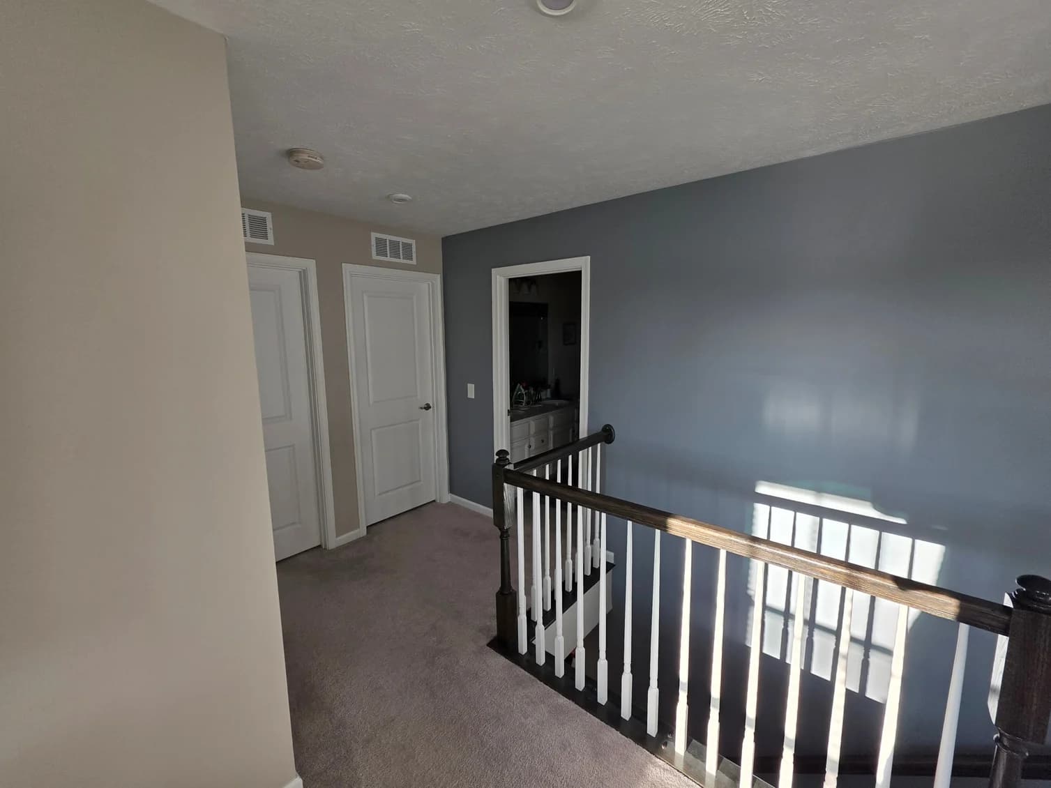 This is an image from Resurrection Painting LLC, located in Ohio. The image shows a freshly painted upstairs hallway with gray and neutral-toned walls, white interior doors, stair railing, and smooth, even interior paint coverage.