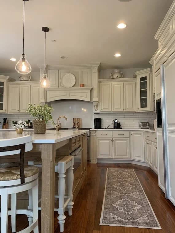 Cabinet painting project by Fulton Revivals in Chicago, IL. The image shows white kitchen cabinets, pendant lights, a patterned runner, and a narrow island.