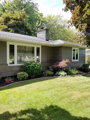 This is an image from Painting Plus Professionals, located in California. The image shows a single-story home exterior with newly painted siding, white-framed windows, and clean landscaping around the foundation.