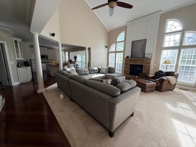 Interior painting project by Norby Painting - CLT in Charlotte, NC. The image shows a living room with high ceiling, arched windows, gray sectional, and fireplace.