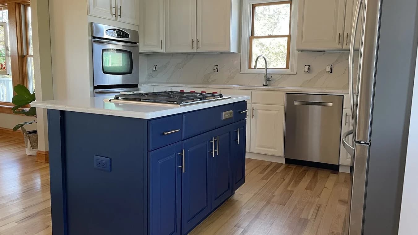 Cabinet painting project by Kitty Hawk Painting in Kitty Hawk, NC. The image shows a kitchen with a navy island, white cabinets, and wood flooring.