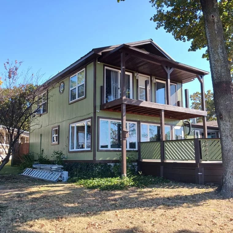 Two-story home with green siding and brown trim painted by Remarkable Painting, featuring a covered balcony and numerous windows with fresh, clean lines.