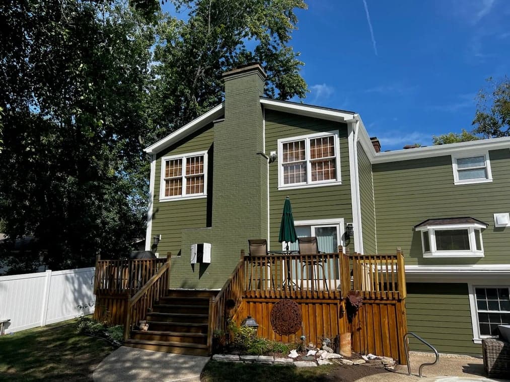 Exterior painting by Affordable Interior & Exterior Painting in Glen Ellyn, Illinois. The image shows green siding, white trim, a chimney, and a wood deck.