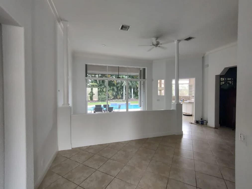 This is an image from Promax Painters company, located in Boynton Beach, FL. The image is an interior living space with fresh white paint, tile flooring, decorative columns, and large window view of backyard pool