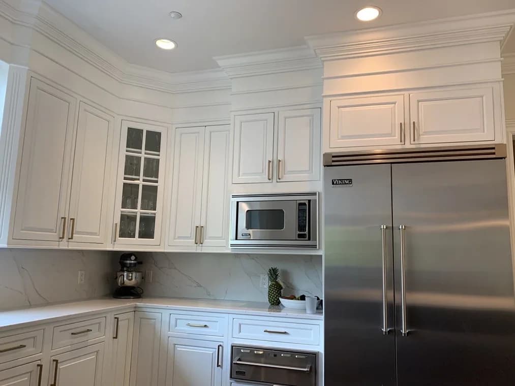 This is an image from C.E.T. Painting, located in New York. The interior photo displays a white kitchen with custom cabinetry, crown molding, and stainless steel appliances.