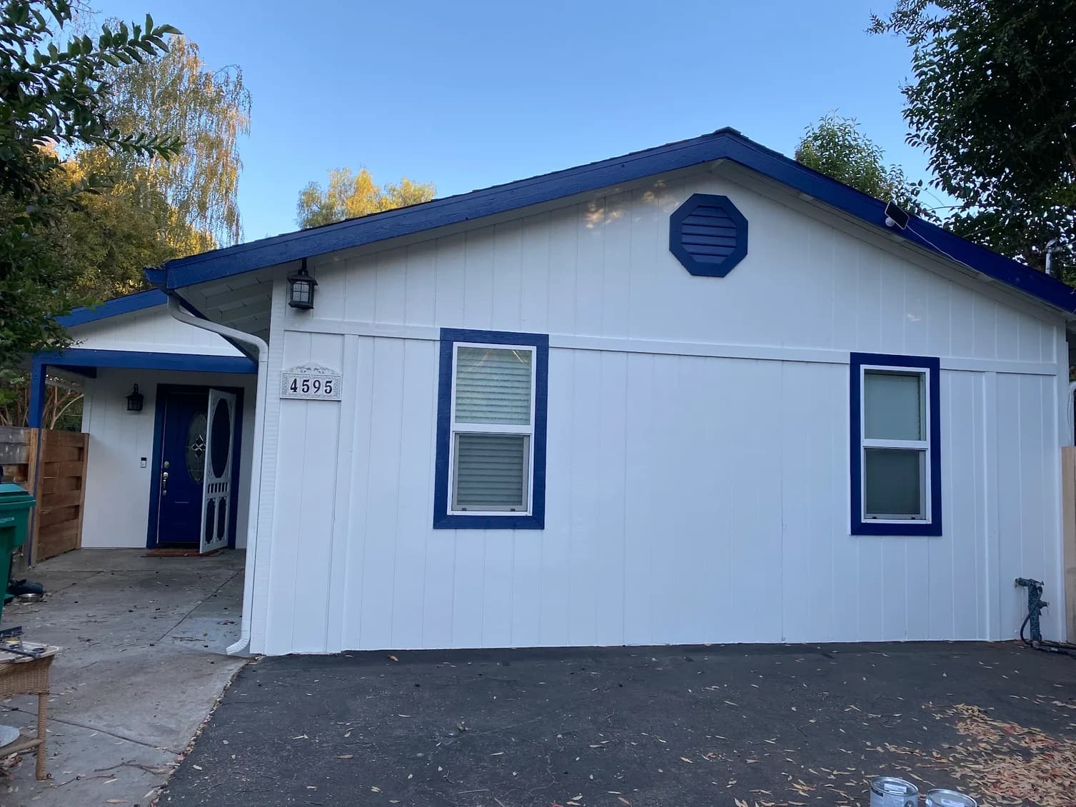 This is an image from Browder Painting Company, located in California. The image shows a freshly painted single-story home exterior with white vertical siding, blue trim accents, a blue front door, and a clean modern finish.
