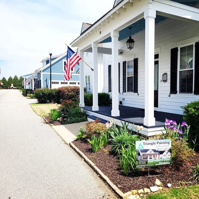 Exterior painting project by Triangle Painting And Drywall llc in Raleigh, NC. The image shows a white porch with blue ceiling, black shutters, columns, plants, and a yard sign.