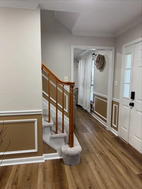 This is an image from Santana Painting Co, located in Maryland. The hallway photo displays painted wall paneling, a wooden staircase with carpeted steps, and light wood-tone flooring.