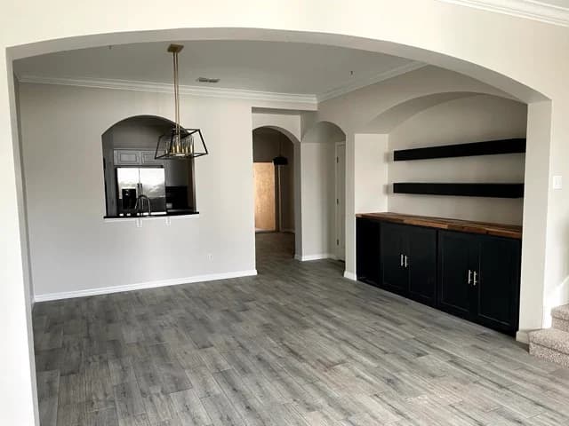 This is an image from TopBrush Painting company, located in Altamonte Springs, FL. The image is a modern living room with fresh light beige paint, arched doorways, gray wood-look tile flooring, black built-in shelving, and contemporary pendant light