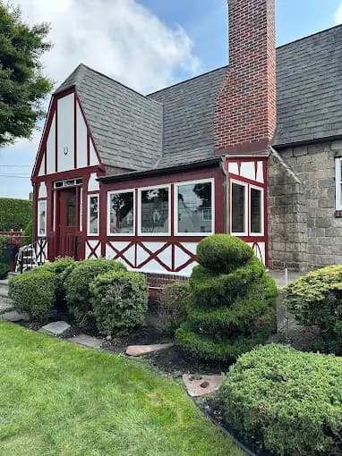 This is an image from Teall Painting, located in Michigan. The image shows a detailed exterior house painting with red and white trim, stone accents, and neatly maintained landscaping around the home.