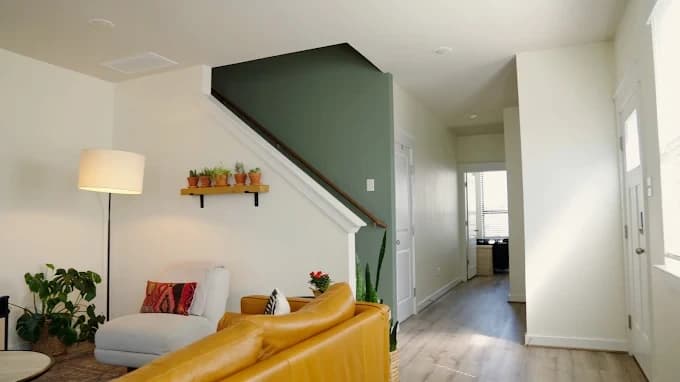 Interior painting project by That 1 Painter Charlotte - Fort Mill in Charlotte, NC. The image shows a green stair wall, yellow sofa, white walls, and wood flooring.