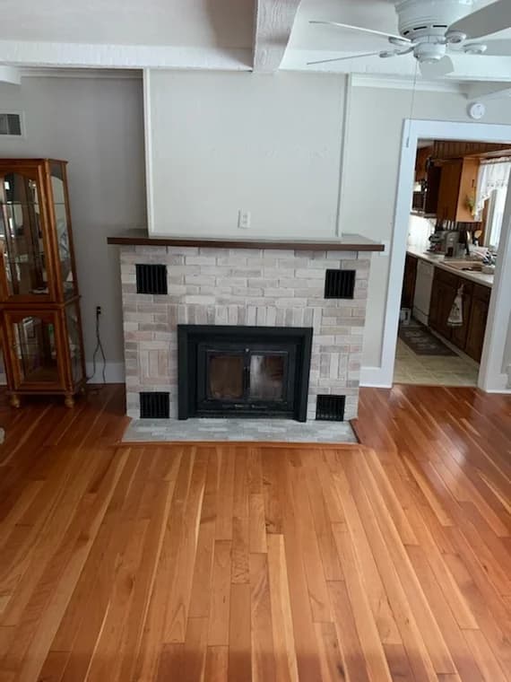 This is an image from Braun's Painting, LLC, located in New York. The image shows a painted brick fireplace with a wood mantel and polished hardwood floors in a living space.