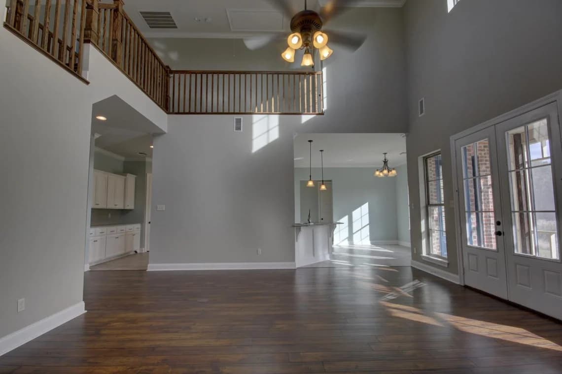 This is an image from Schmidt Painting, located in Massachusetts. It highlights an interior of a modern two-story home with freshly painted neutral gray walls by Schmidt Painting, complemented by dark hardwood floors and ample natural light.