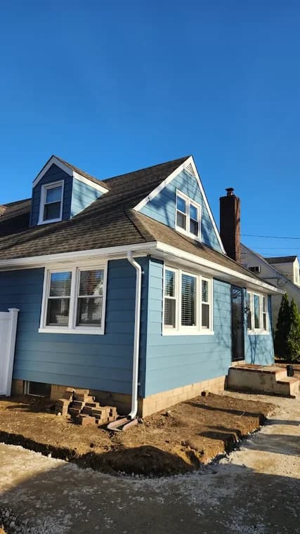 This is an image from CRD Painting Inc, located in New York. The photo shows a freshly painted blue two-story home exterior with white trim and new siding work under clear daylight.