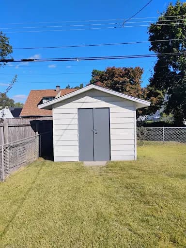 This is an image from Disbrow Painting And Handyman Services Company company, located in Levittown, PA. The image is recently painted light gray shed with dark gray doors in a residential backyard.