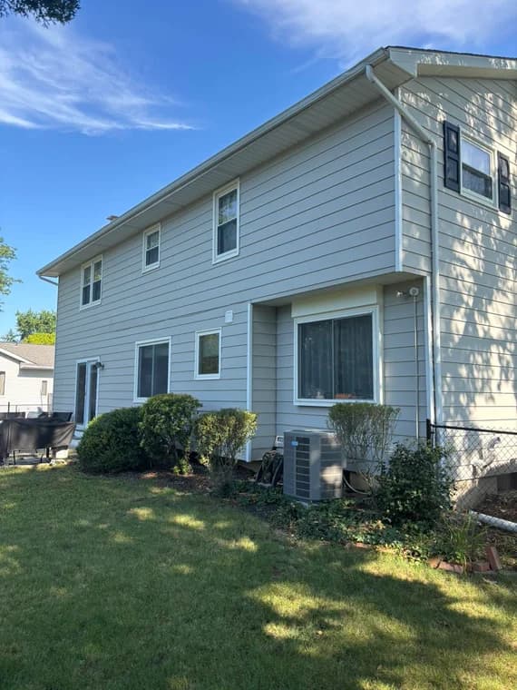 A light gray two-story house with black shutters freshly painted by WallPro Painting & Design, showcasing a clean modern look against a bright blue sky.