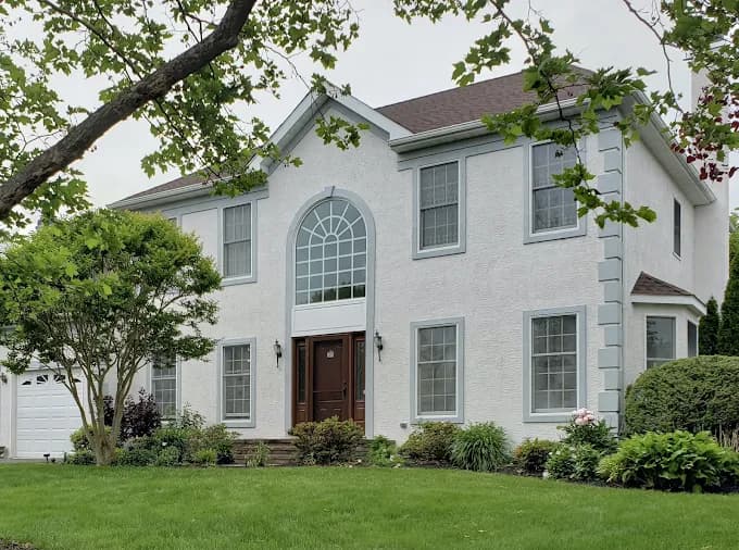 This is an image from T Whitaker Painting in New Jersey. It shows the exterior of a freshly painted two-story home with white siding and elegant trim.