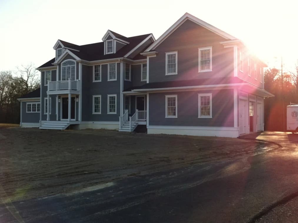 This is an image from Nelson Painting, Inc., located in Massachusetts. It displays a large two-story home with blue-gray siding, white trim, and detailed exterior finish work under natural sunlight.