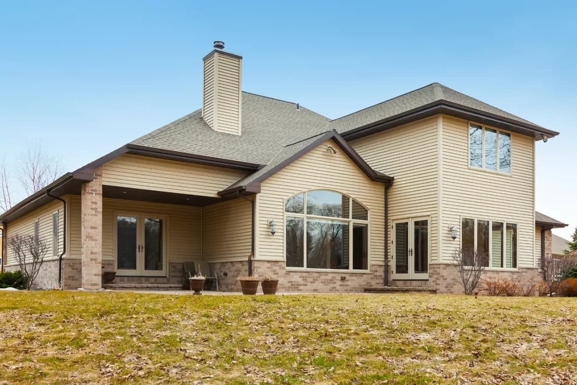 "This is an image from CertaPro Painters of Lake Ray Hubbard, located in Texas. The photo shows a large beige two-story home with vinyl siding and brick accents viewed from the backyard."