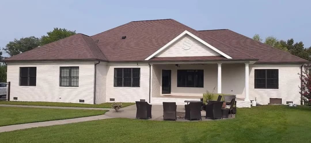 This is an image from Triple G Custom Painting Drywall & Roofing LLC, located in Indiana. The exterior of a large single-story home is painted white with black window trim and a brown roof, showing a freshly completed exterior painting project.
