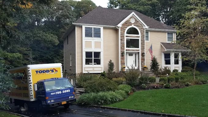 This is an image from Todd's Painting, located in New York. The exterior of a beige two-story home is shown alongside a Todd's Painting power washing truck parked in the driveway.