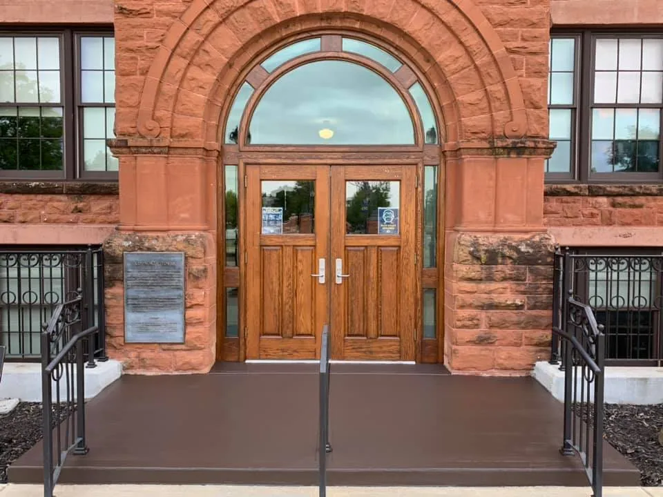 This is an image from Legacy Painting, located in Edmond, Oklahoma. The restored entrance of a historic stone building shows a wooden double door framed by detailed red sandstone archways.