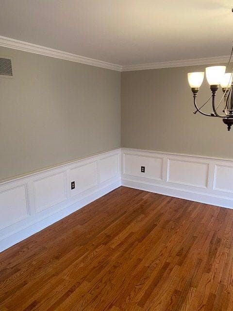This is an image from Pizzazz Painting, showing a dining room with light gray walls, white wainscoting, and hardwood floors under a chandelier.