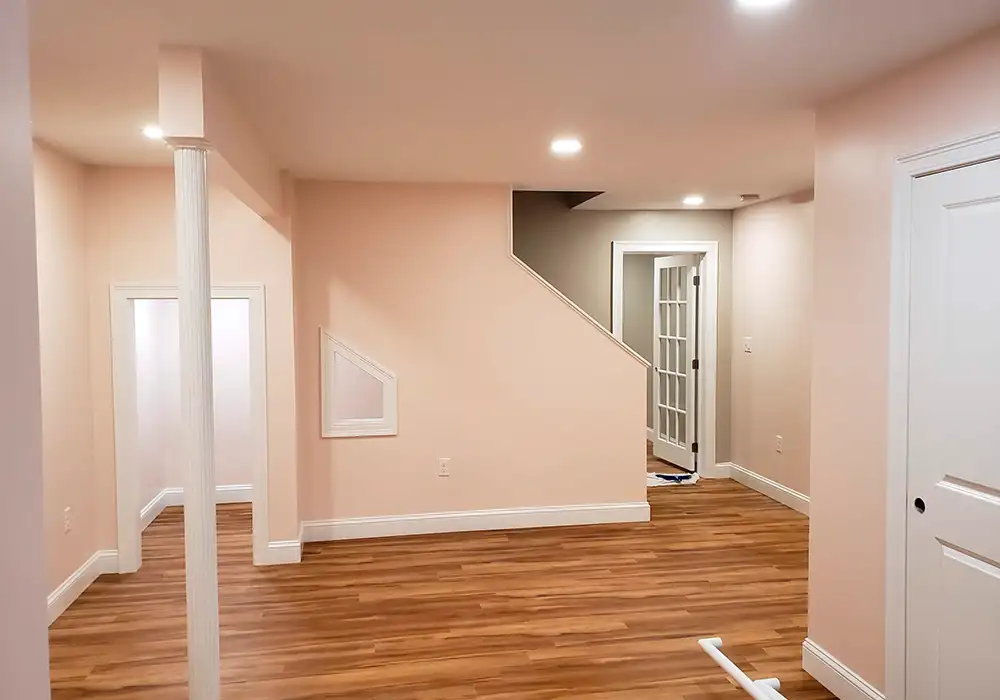 This is an image from Zuck Painting, located in Massachusetts. It shows a finished basement interior with light peach-colored walls, crisp white trim, and wood-style flooring.