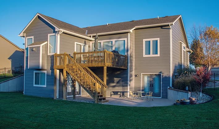 This is an image from CertaPro Painters of Wichita East KS. The image is a two-story gray home in Wichita KS with newly painted siding and a raised wooden deck.