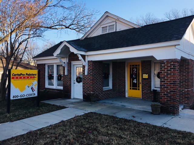 "This is an image from CertaPro Painters of Lake Ray Hubbard, located in Texas. The photo shows a small brick commercial-style building with white trim, a yellow front door, and a CertaPro Painters yard sign in front."