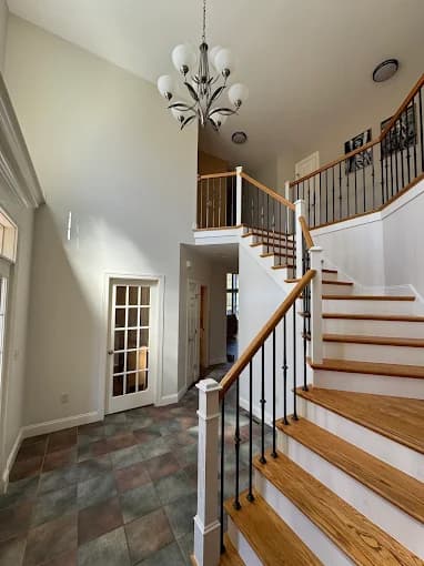 This is an image from Joseph Rivers Painting, located in Ohio. The image shows a residential entryway with a staircase, wood steps, black metal railings, and tiled flooring beneath a hanging chandelier.