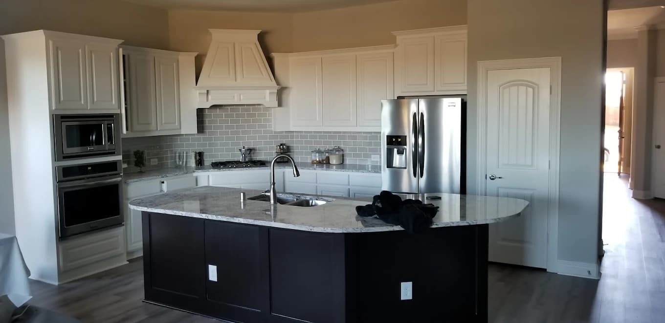 "This is an image from Texas Star Painting, located in Texas. The modern kitchen features white upper cabinets, a dark island base, stainless-steel appliances, and light gray subway tile backsplash."