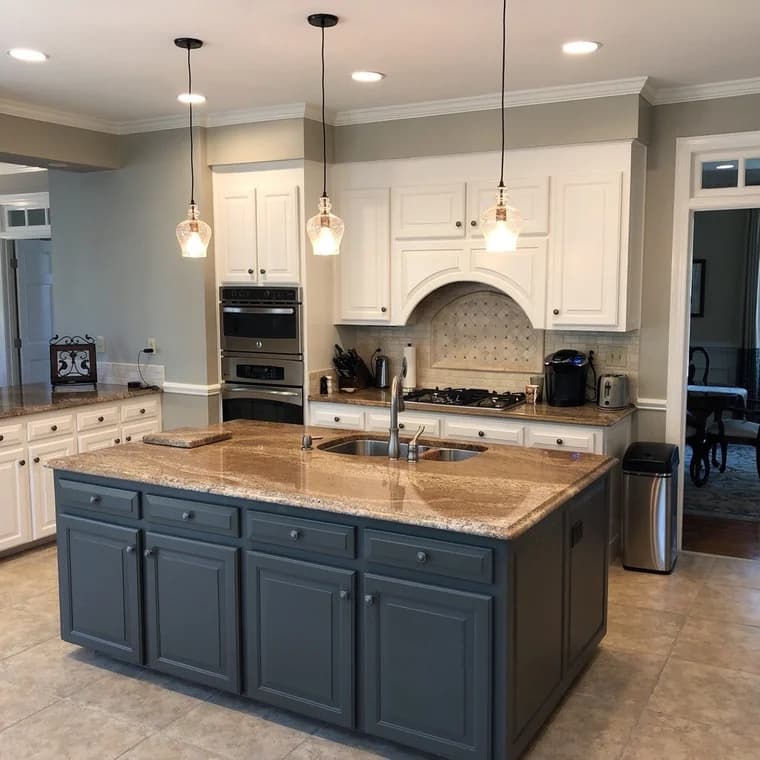 Cabinet painting project by Anderson Painting in Raleigh, North Carolina. The image shows white cabinets, a gray island, counters, and pendant lights.