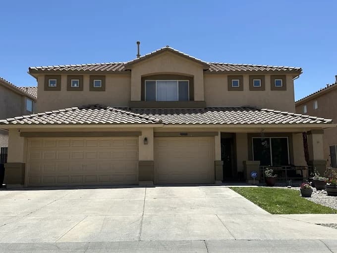 This is an image from New Mexico's Painting Specialists, located in New Mexico. The image shows a two-story tan stucco home with a tiled roof, freshly painted trim, and a three-car garage under a clear blue sky.
