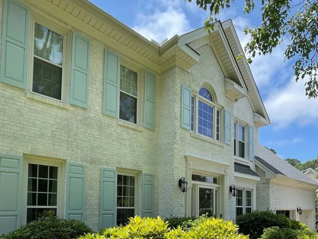 Painting work by Oak City Coatings in Raleigh, North Carolina. The image shows a whitewashed brick home with dark shutters.