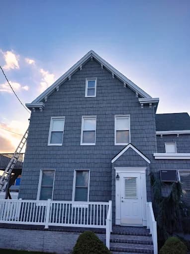 This is an image from Big Expert Painting LLC, located in New York. The exterior image shows a gray-painted multi-story home with white trim, a white front door, and a matching white railing along the porch.
