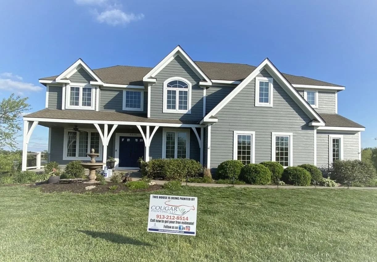 This is an image from Cougar Painting LLC. The image is exterior home in Kansas City KS with freshly painted gray siding, white trim, and a Cougar Painting yard sign.