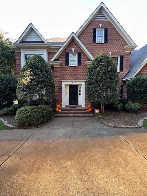 Exterior painting project by GW Painting in Charlotte, NC. The image shows a red brick two-story home with white trim and front shrubs.