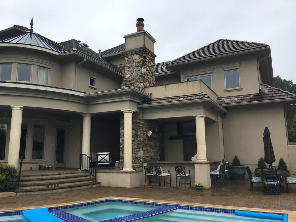 Exterior coating project by Rhino Shield Carolina in Charlotte, NC. The image shows a tan stucco home with stone chimney, covered patio, and pool.