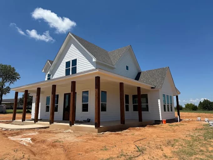 This is an image from Whitehead Brothers Painting, located in Oklahoma. The exterior photo shows a newly painted white farmhouse with dark wood porch posts, a gray roof, and wide windows under a clear blue sky.