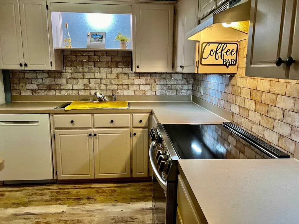 This is an image from Family Painting, located in Texas. The photo shows a kitchen with freshly painted beige cabinets, updated countertops, and a stone-pattern backsplash.