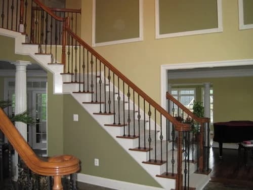 This is an image from CertaPro Painters of Columbia, located in Maryland. The photo shows a freshly painted interior staircase with green walls, white trim, and a wooden handrail with black wrought-iron spindles.