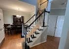 Interior trim painting project by Recinos Painting in Apex, NC. The image shows a staircase with white balusters, dark rails, wood floors, and light walls.