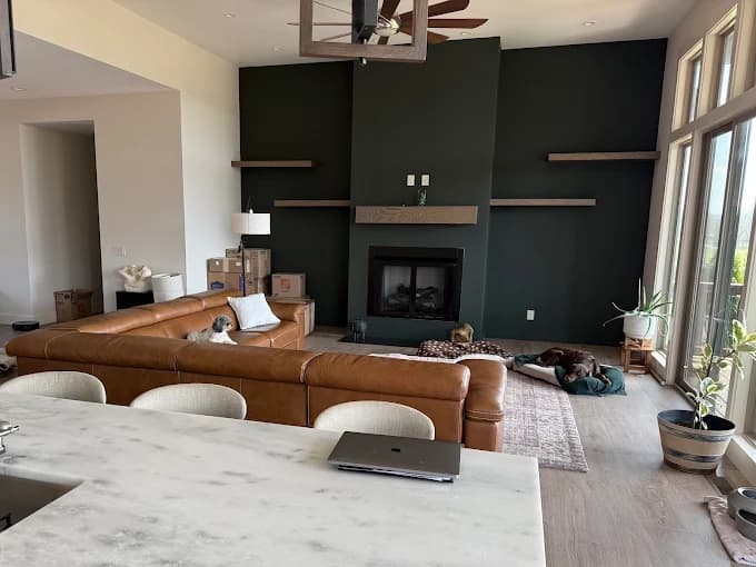 Interior painting project by Burlett Painting, LLC in Hendersonville, North Carolina. The image shows a dark fireplace wall, brown sofa, and tall windows.