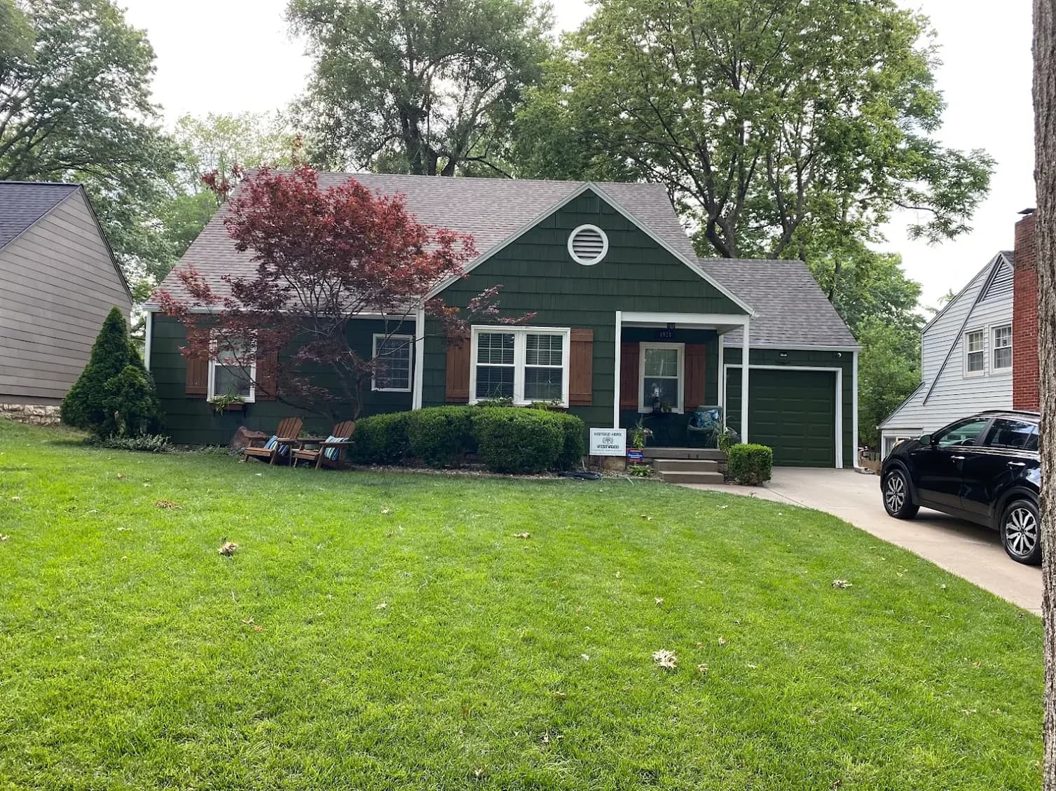 This is an image from Stone Painting. The image shows a green home with wood shutters, a front porch, and a large tree shading the front yard.